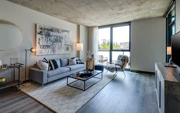 A modern living room with a grey sofa, a coffee table, and a large abstract painting on the wall. at The Mason Apartments, Chicago, Illinois