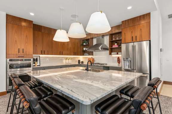 A modern kitchen with a marble island and black barstools.