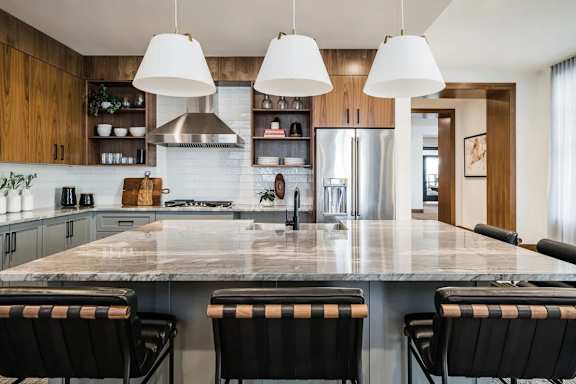 A kitchen with a marble countertop and black barstools.