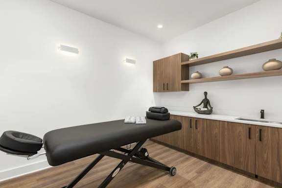 A massage table in a room with wooden shelves and a chair.