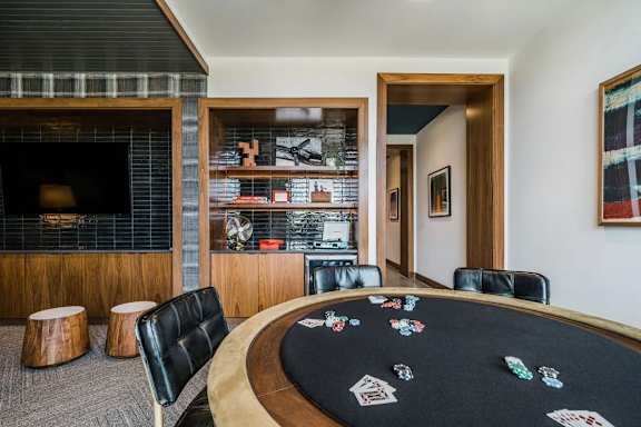 A poker table with chips and cards is surrounded by black leather chairs.