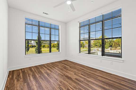 A room with wooden floors and two windows with blinds.