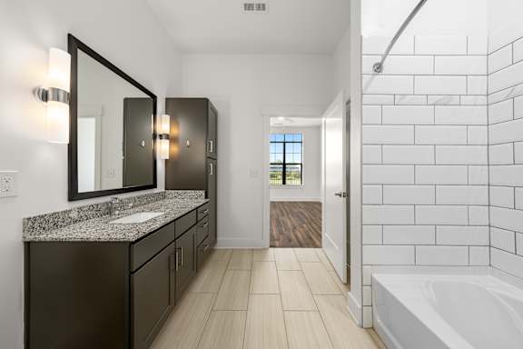 A bathroom with a white tub and a sink with a granite counter.