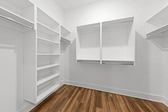 A white walk in closet with shelves and a wooden floor.