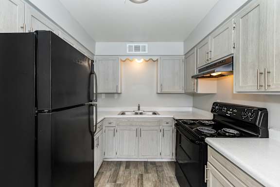 A black refrigerator stands next to a black stove in a kitchen with white cabinets.