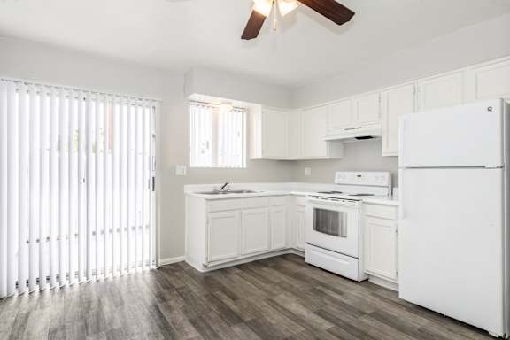 A white kitchen with wood flooring and a ceiling fan.