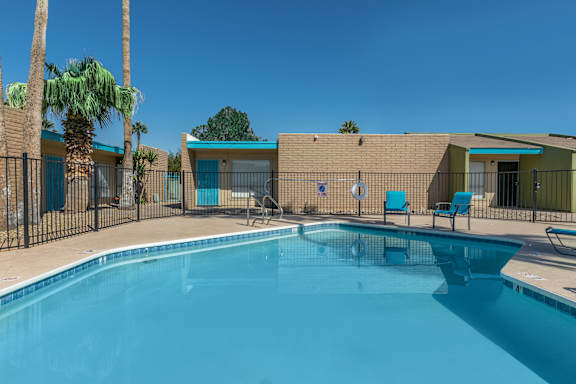 A swimming pool surrounded by a fence with palm trees in the background.