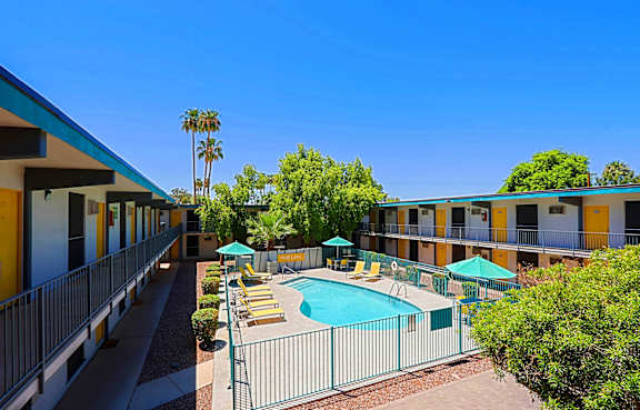 A pool surrounded by chairs and umbrellas is in front of a building with balconies.
