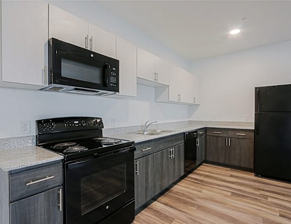 A kitchen with black appliances and wooden floors.