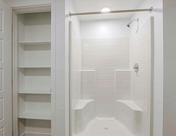 A white tiled shower with a glass door and a white cabinet.