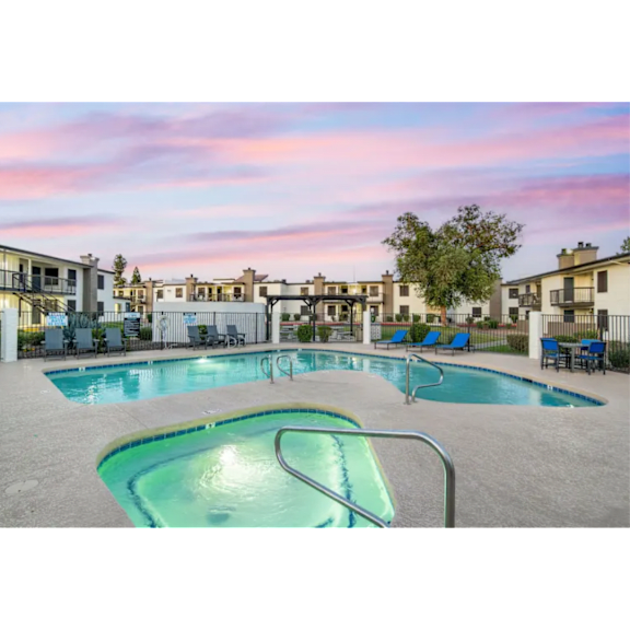 A swimming pool surrounded by lounge chairs and apartment buildings in the background.