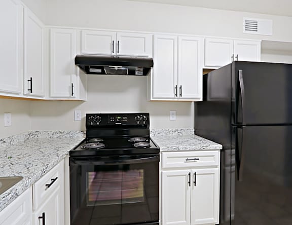 A black stove and refrigerator in a kitchen with white cabinets.