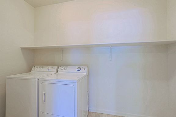 Two white washing machines in a white room.
