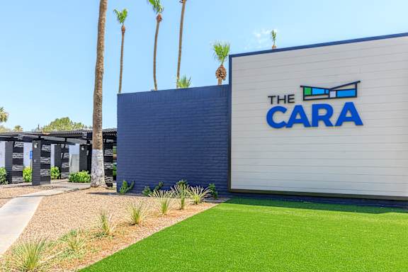 A building with a sign that says "The Cara" in front of some palm trees.