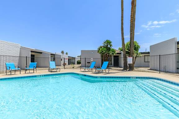 A swimming pool surrounded by chairs and a fence.