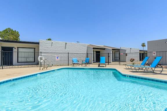A swimming pool in front of a building with blue lounge chairs.