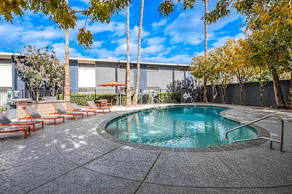 A pool surrounded by trees and chairs.