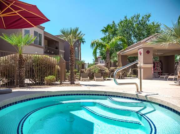 A pool with a red umbrella and a building in the background.