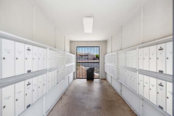 A long hallway with white lockers on both sides and a black trash can at the end.