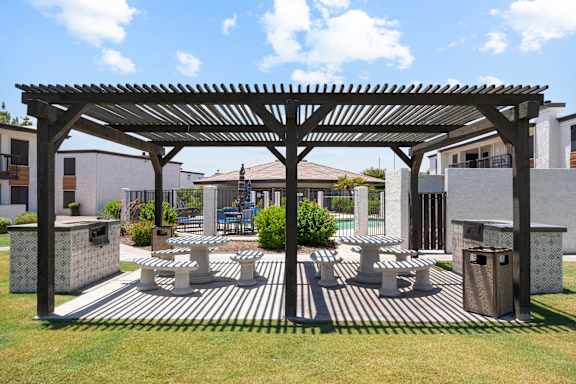 A wooden pergola with a striped concrete floor and a grassy area in front.