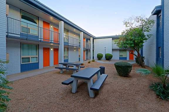 A courtyard with a picnic table and a hedge in front of apartment buildings.