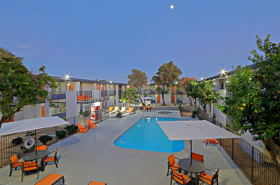 View of soothing swimming pool with orange patio furniture at twiligjht at Allora Phoenix in Phoenix, AZ