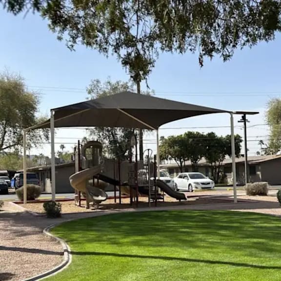 A playground with a slide and a canopy is surrounded by green grass.