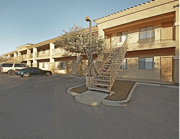 A car is parked in a parking lot in front of a building with a tree and a staircase.