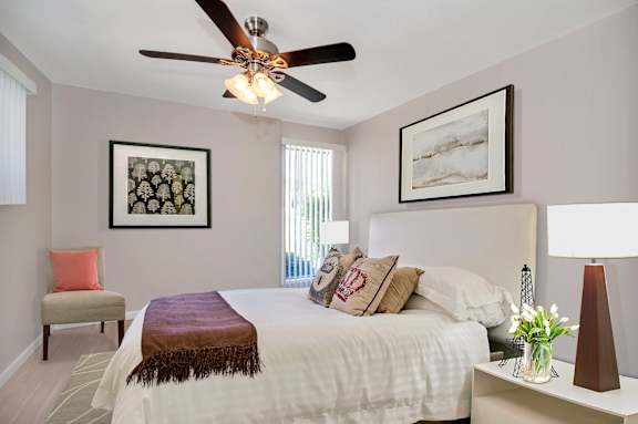 A bedroom with a bed, a chair, a ceiling fan, and two pictures on the wall.