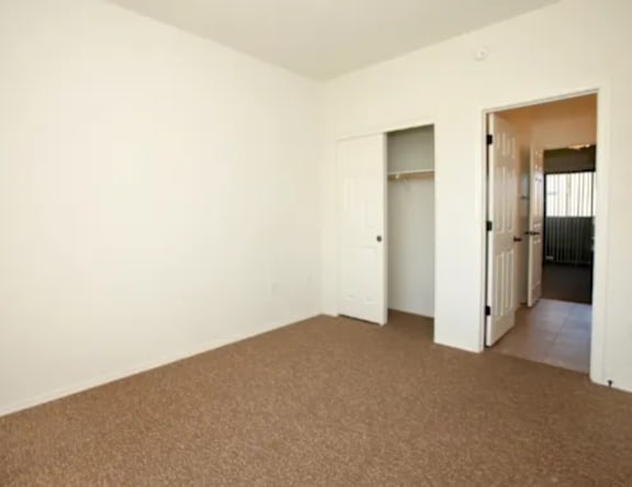 A room with carpeted floor and white walls with three doors.