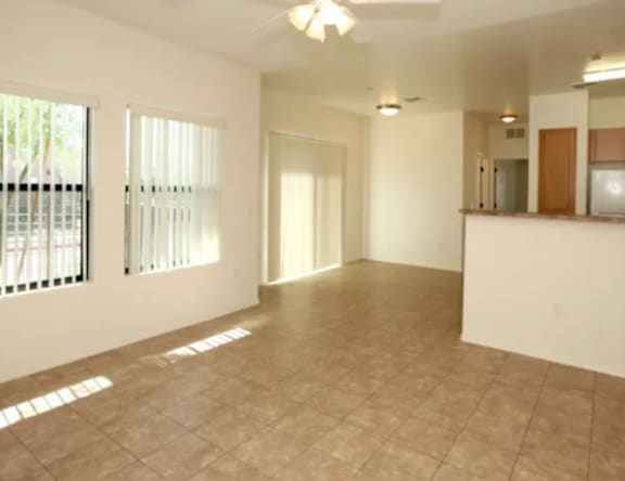 A spacious room with tiled flooring and a large window with blinds.