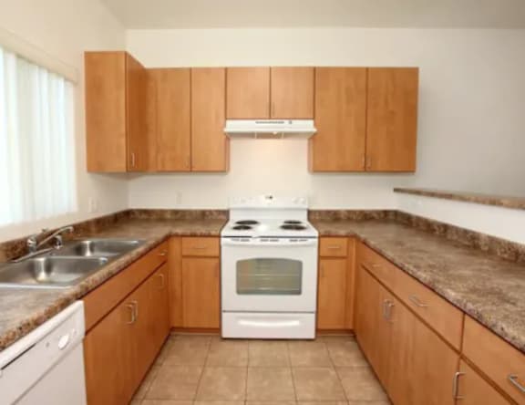 A kitchen with a white stove top oven and wooden cabinets.