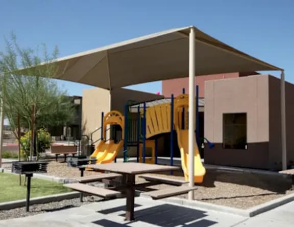 A playground with a yellow slide and a picnic table.