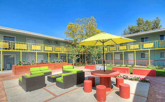 A yellow umbrella sits in the middle of a courtyard with red and green seating.