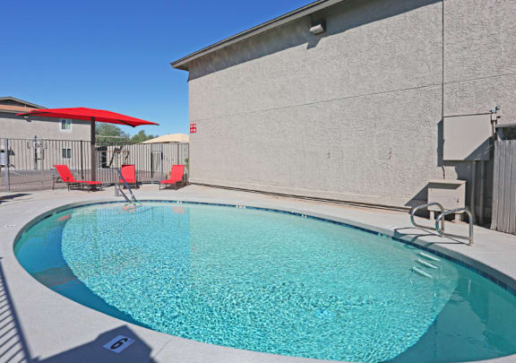 A small pool with a red umbrella and two chairs.
