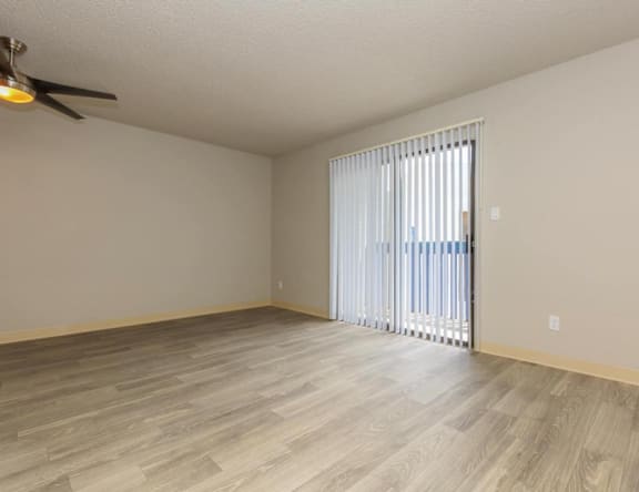 A room with a ceiling fan and light, wooden flooring, and a sliding glass door.