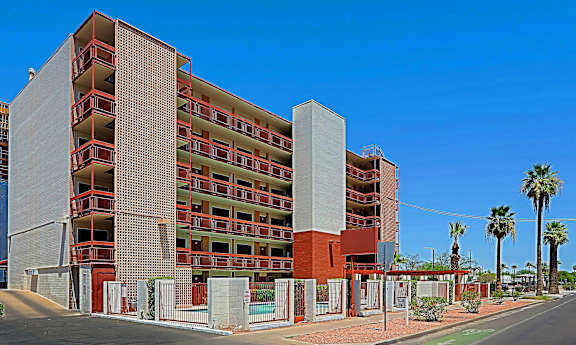 A large red and white building with balconies and a tall palm tree in front of it.