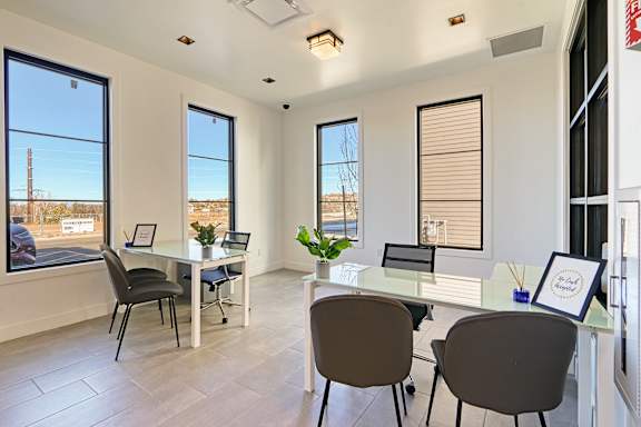 A room with a glass table and chairs, a framed picture, and a window with a view of a building.