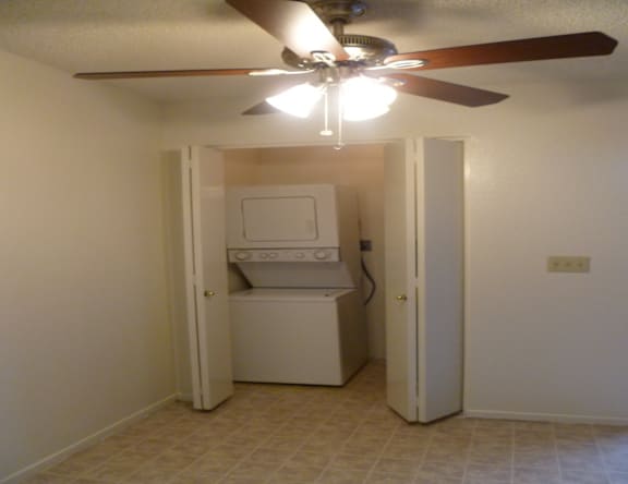 A white washing machine is in a small room with a ceiling fan.