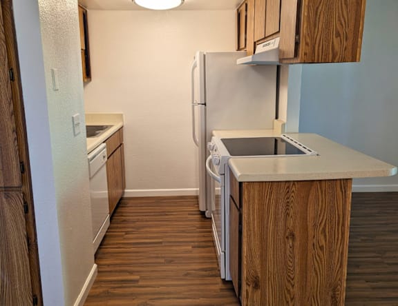 A kitchen with a white refrigerator, wooden cabinets, and a wooden floor.