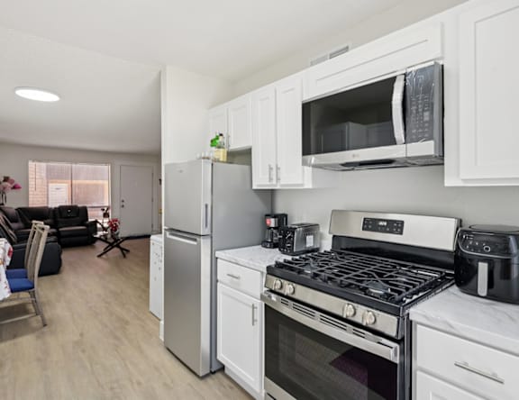A kitchen with white cabinets and appliances, a refrigerator, a microwave, a stove, and a coffee maker.