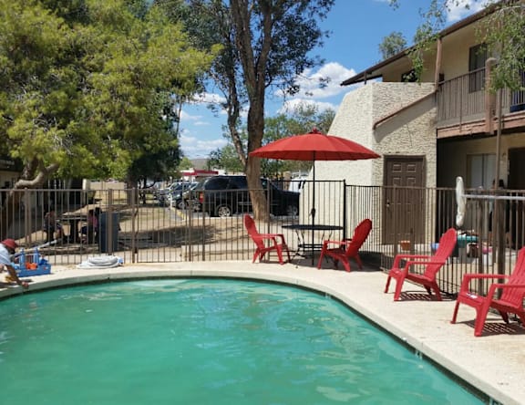 A pool surrounded by red chairs and an umbrella.