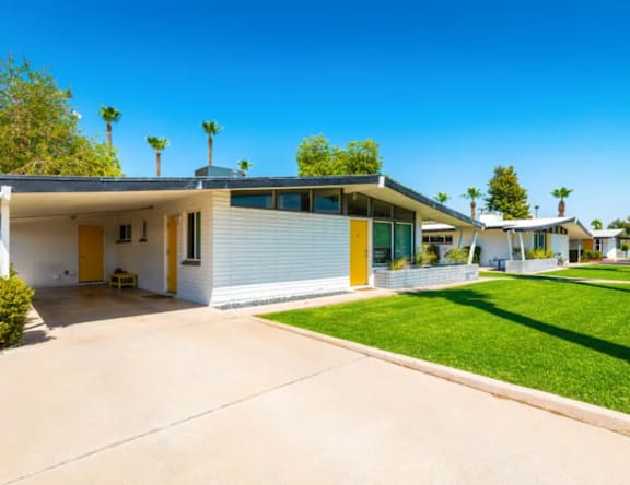 A white house with a yellow door is surrounded by green grass and palm trees.