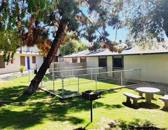 A playground with a swing set and picnic tables is surrounded by a fence and trees.