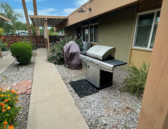A grill is on a gravel area in front of a house.