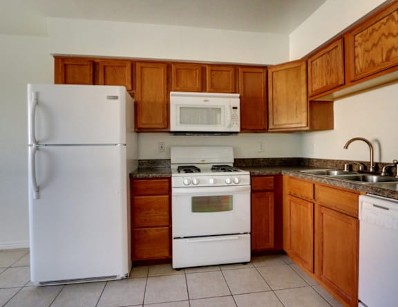 A white refrigerator stands next to a white oven in a kitchen with wooden cabinets.
