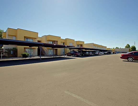 A parking lot with a red car and a building with yellow walls.