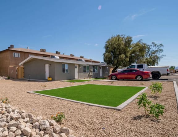 A red car is parked in front of a house with a green lawn.
