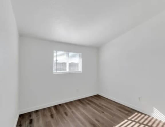 A room with wooden flooring and a window with blinds.