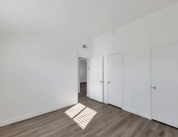 A room with white walls and wooden flooring with a white door in the background.